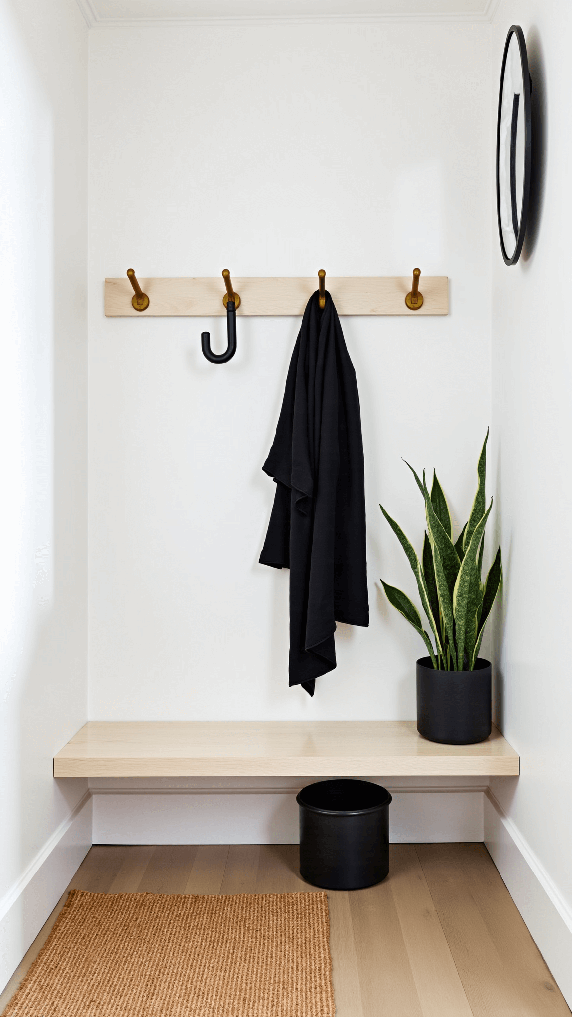 Entryway with whitewashed oak bench, matte black ceramic umbrella stand, brass hooks holding black linen coat, a potted snake plant, and a wall-mounted mirror reflecting natural light