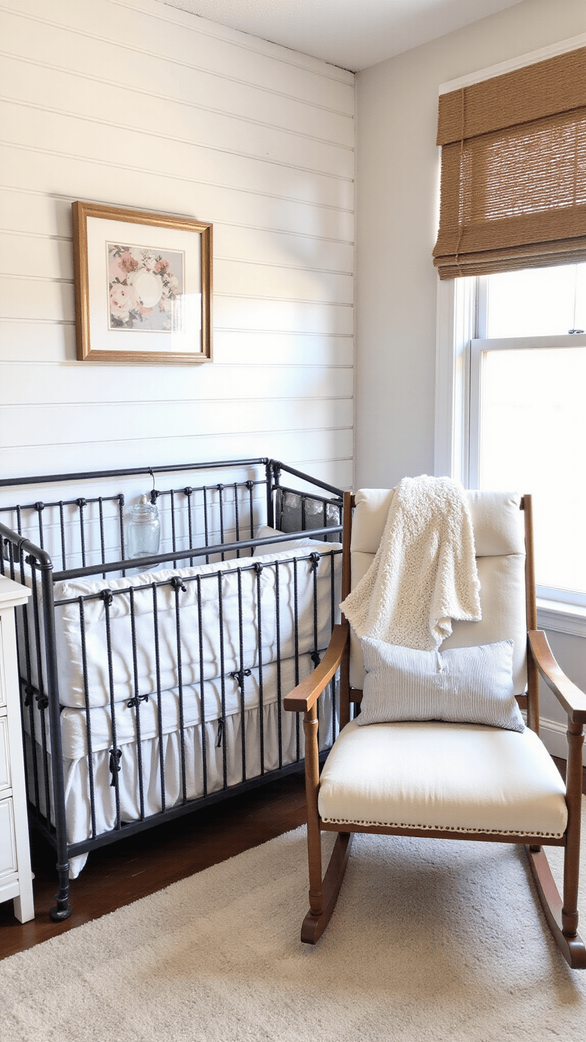 Charming farmhouse nursery with afternoon light highlighting vintage iron crib, distressed white dresser, and wooden rocking chair in a warm white shiplap accented room.